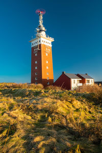 Lighthouse on field against clear blue sky