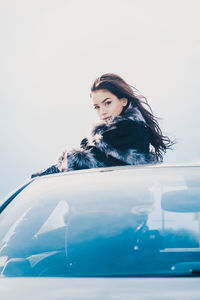 Portrait of young woman looking through sun roof against clear sky