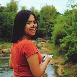 Portrait of woman holding mobile phones while standing by stream