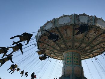 Low angle view of people sitting on chain swing ride against sky