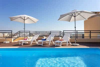 Deck chairs by swimming pool against clear blue sky