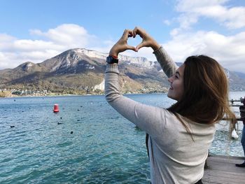 Young woman standing by sea against mountains