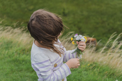 Girl holding flowers while standing on land