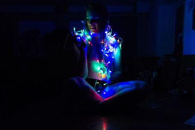 Young woman with illuminated string lights sitting at home