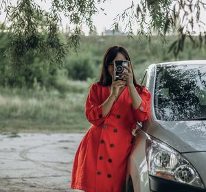 A girl in a red dress parked her car in nature by the river.