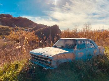 Abandoned car on by plants on land against sky