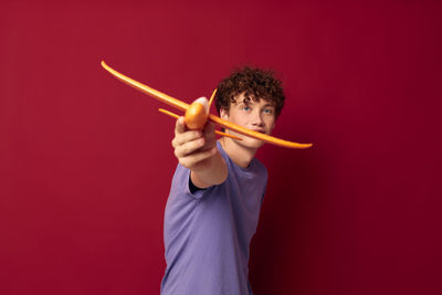Portrait of young man holding model airplane against red background