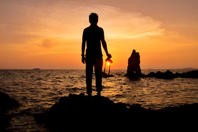 Silhouette man standing on rock at beach during sunset