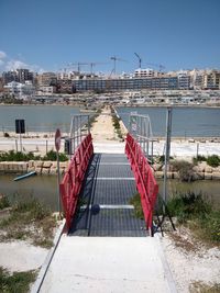 Bridge near seaside against buildings in city against sky