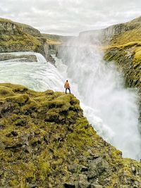 Man standing on rock against waterfall