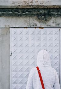 Rear view of person in hood standing against wall