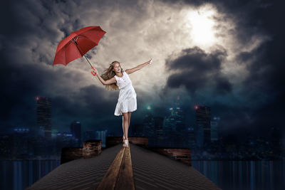 Digital composite image of woman holding umbrella on roof at night