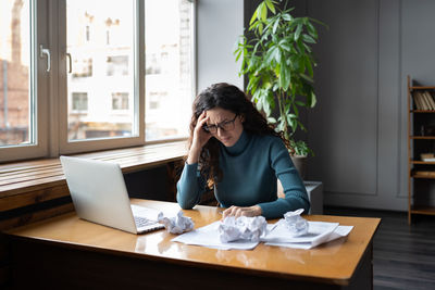 Overwhelmed tired businesswoman sit at desk with laptop and crumpled paper frustrated and exhausted