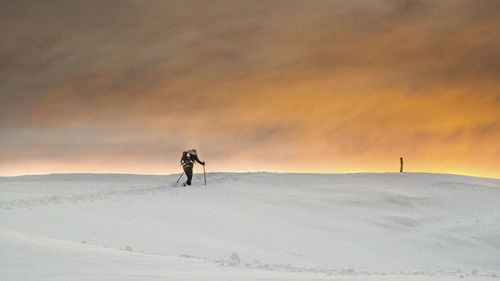 Man on snow covered land against sky during sunset