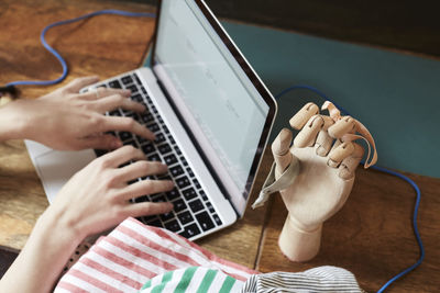 Cropped image of podcaster typing on laptop by hand mannequin with hair elastics at table