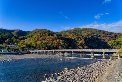 Bridge over river by trees against blue sky