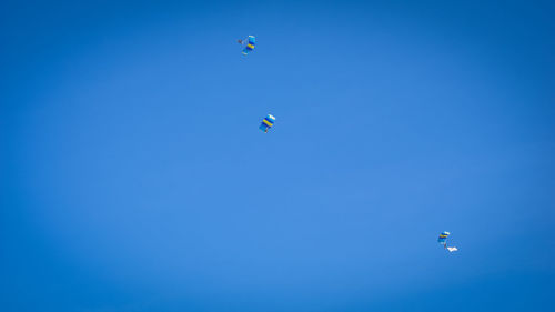 Low angle view of parachutes flying against clear blue sky