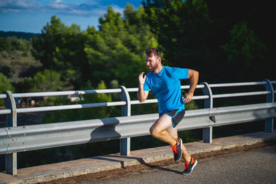 Full length of man running on sidewalk against trees