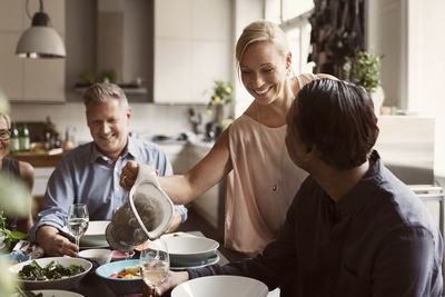 Happy woman serving drink to mature man at table