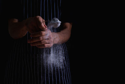 Midsection of man holding drink against black background