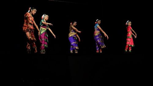 Group of people dancing against black background