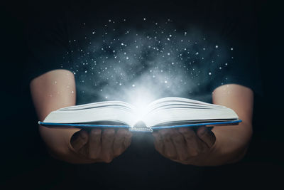 Digital composite image of hand holding book against black background