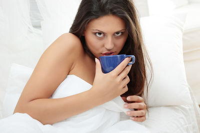Portrait of young woman drinking coffee cup on bed at home