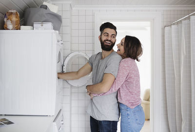 Happy couple standing by washing machine at home