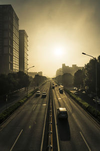 Vehicles on road in city against sky during sunset