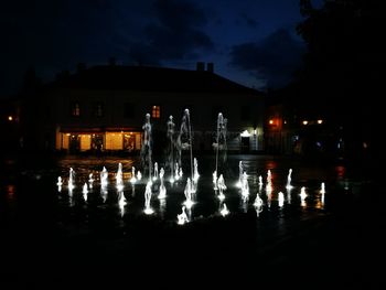 Silhouette buildings by lake against sky at night