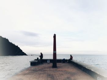 People sitting on pier over sea against sky