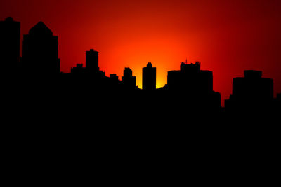 Silhouette buildings against orange sky during sunset