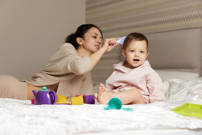 Portrait of mother and daughter sitting on bed at home