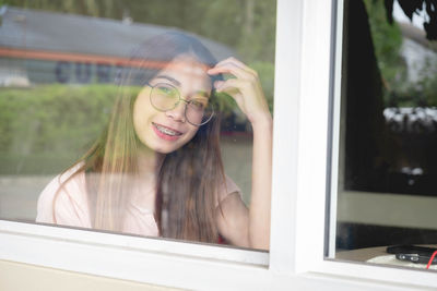 Portrait of smiling young woman seen through glass window