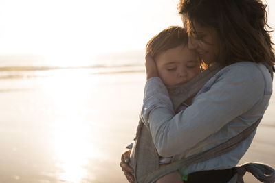 Mother carrying son while standing at beach