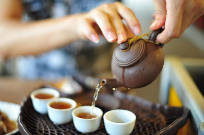 Midsection of man pouring chinese tea from teapot in cup at home