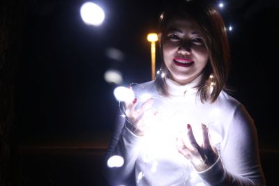 Portrait of smiling woman with illuminated lights in darkroom