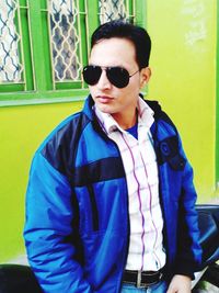 Portrait of young man wearing sunglasses while standing against wall