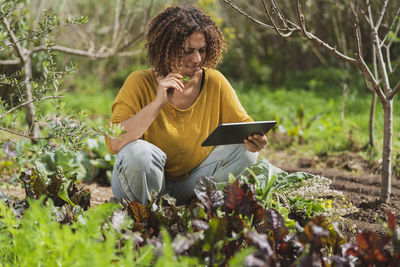 Full length of senior woman using phone while sitting on plants