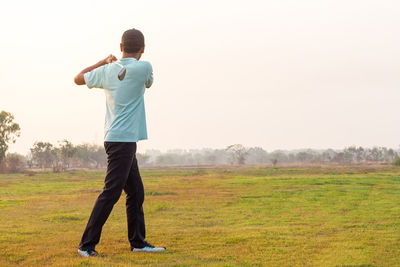 Rear view of man standing on field against clear sky