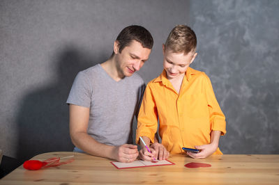 Happy boy and dad sign a valentine's day card and laugh sitting at the table