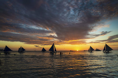 Silhouette sailboats in sea against dramatic sky during sunset