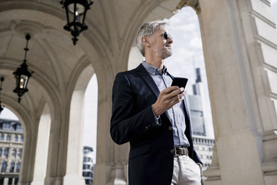Grey-haired businessman in the city holding smartphone