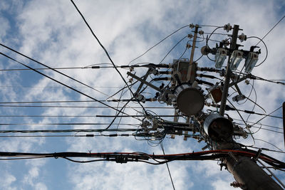 Low angle view of electricity pylon against cloudy sky