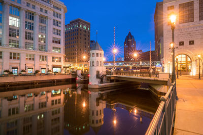 Illuminated bridge over canal by buildings in city at night