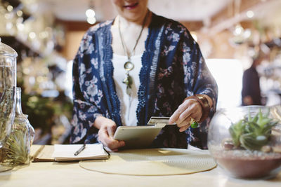 Midsection of owner reading credit card through tablet computer for payment in plant shop