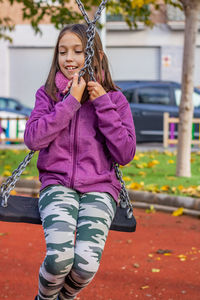 Smiling girl sitting on swing at playground