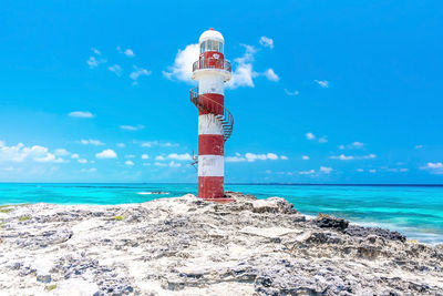 Striped lighthouse on rocky shore of beautiful seascape against sky