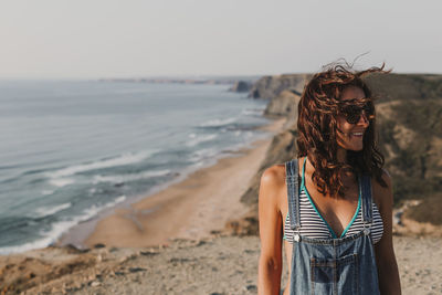 Young woman standing at beach against sky