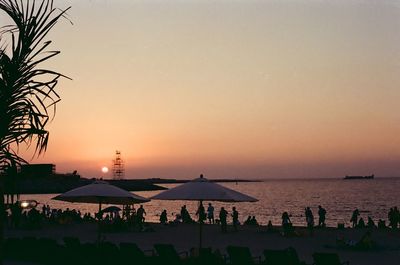 Silhouette people on beach against clear sky during sunset